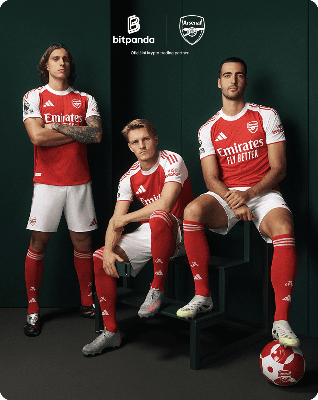 Three soccer players in red and white Arsenal kits pose confidently with a soccer ball, featuring Bitpanda and Arsenal logos in the background.