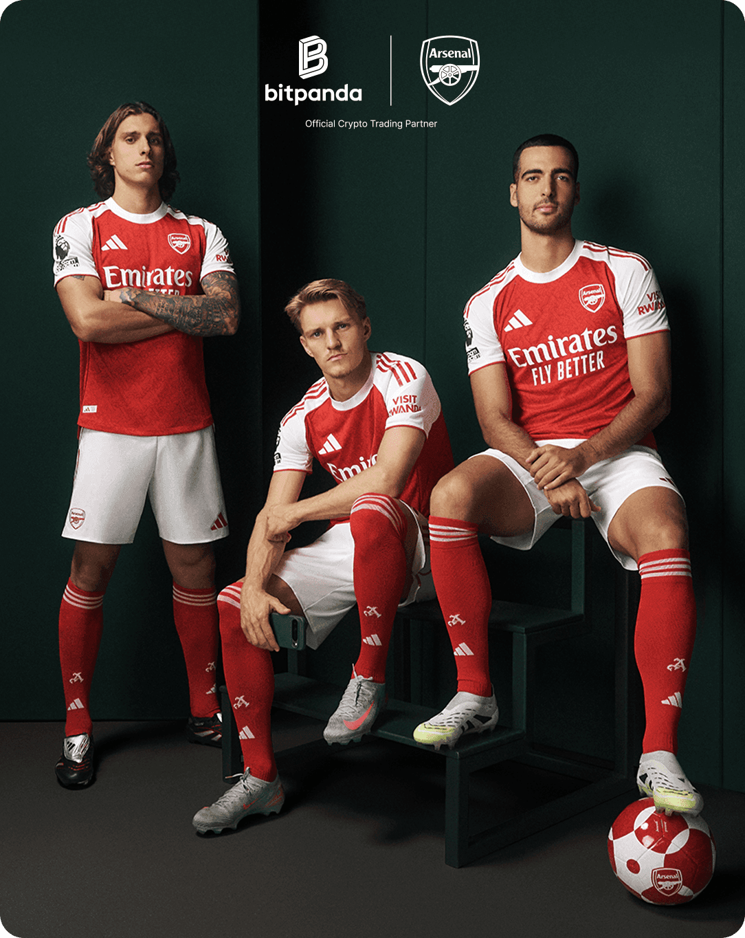 Three soccer players in red and white Arsenal jerseys pose confidently with a ball, showcasing Bitpanda and Arsenal logos in the background.