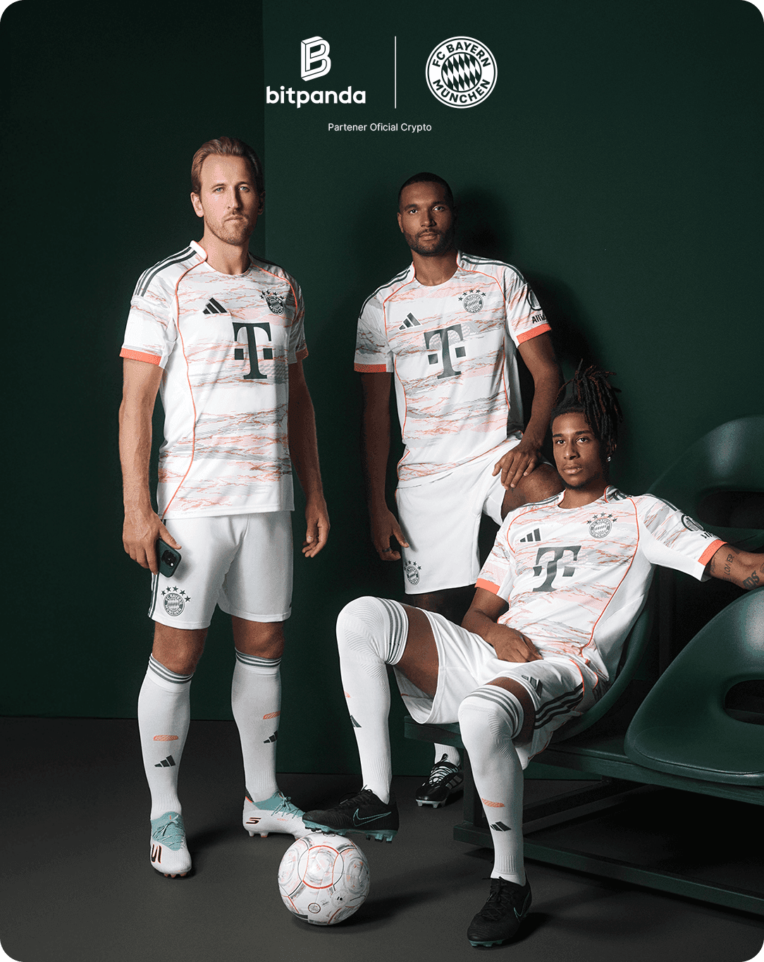Three soccer players in white and orange Bayern Munich jerseys pose with a ball indoors, next to Bitpanda and Bayern Munich logos.