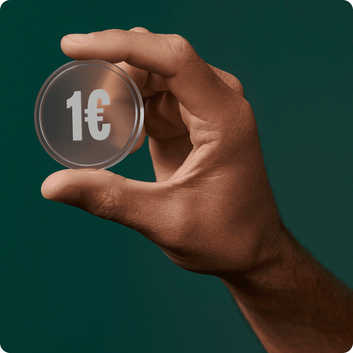 Hand holding a transparent coin with "1€" printed on it against a dark green background.