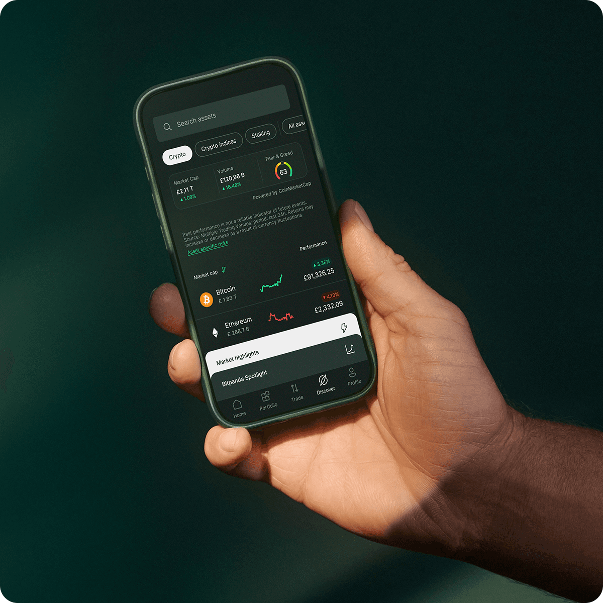 Hand holding a smartphone displaying a cryptocurrency app interface with Bitcoin and Ethereum prices, charts, and market highlights.