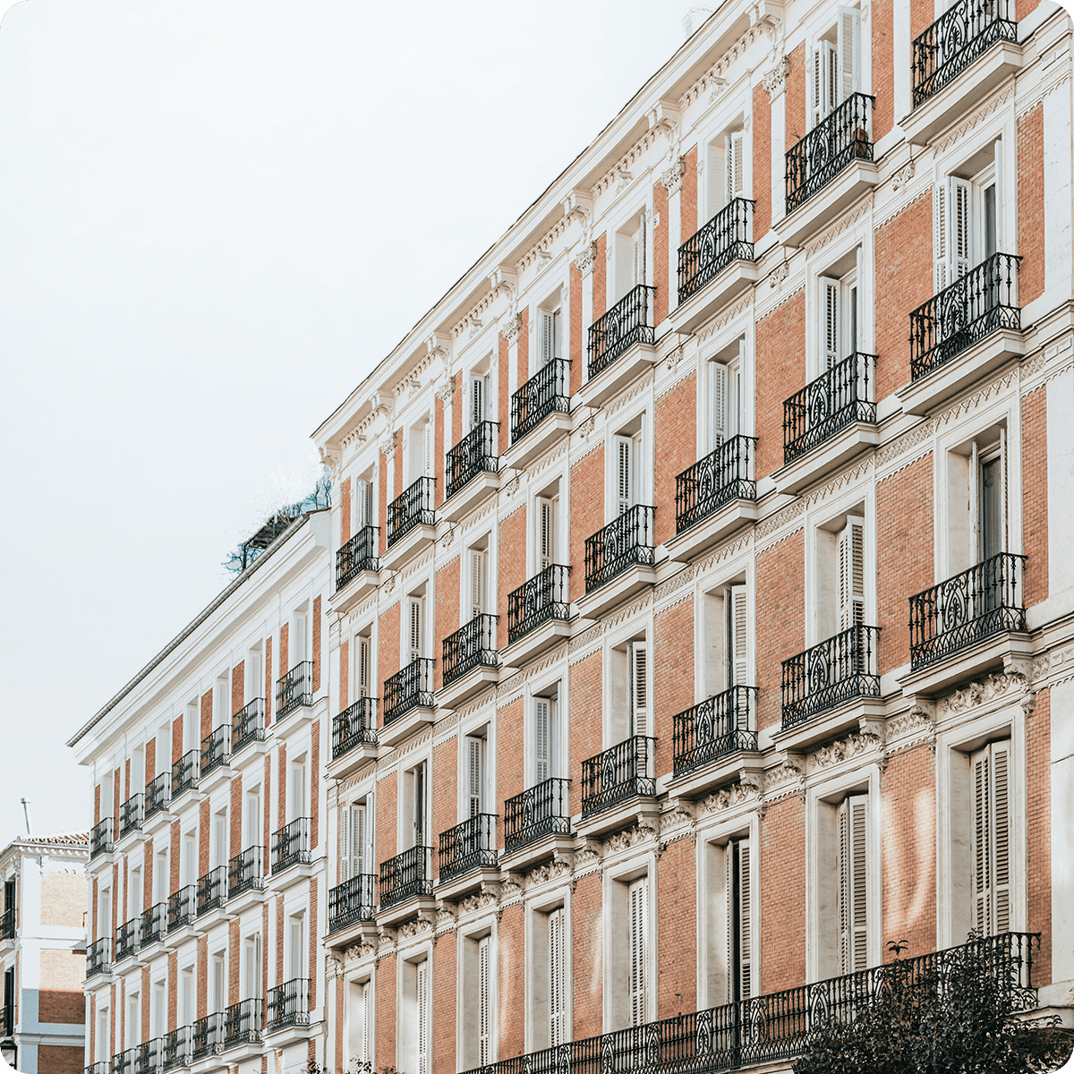 A row of elegant, multi-story brick buildings with white trim and black wrought-iron balconies under a clear sky.