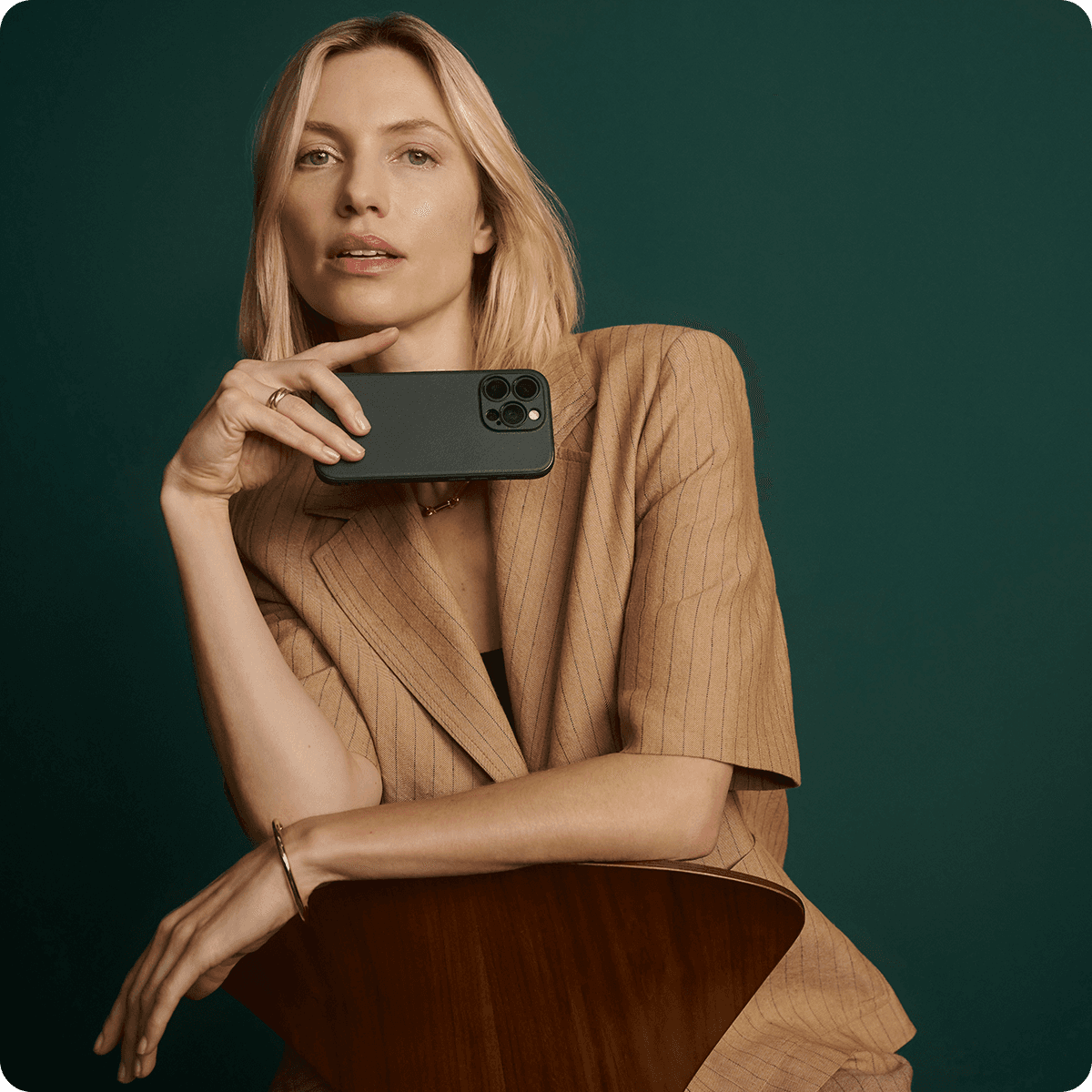 Person with blonde hair in a tan suit holding a smartphone, seated against a green background.