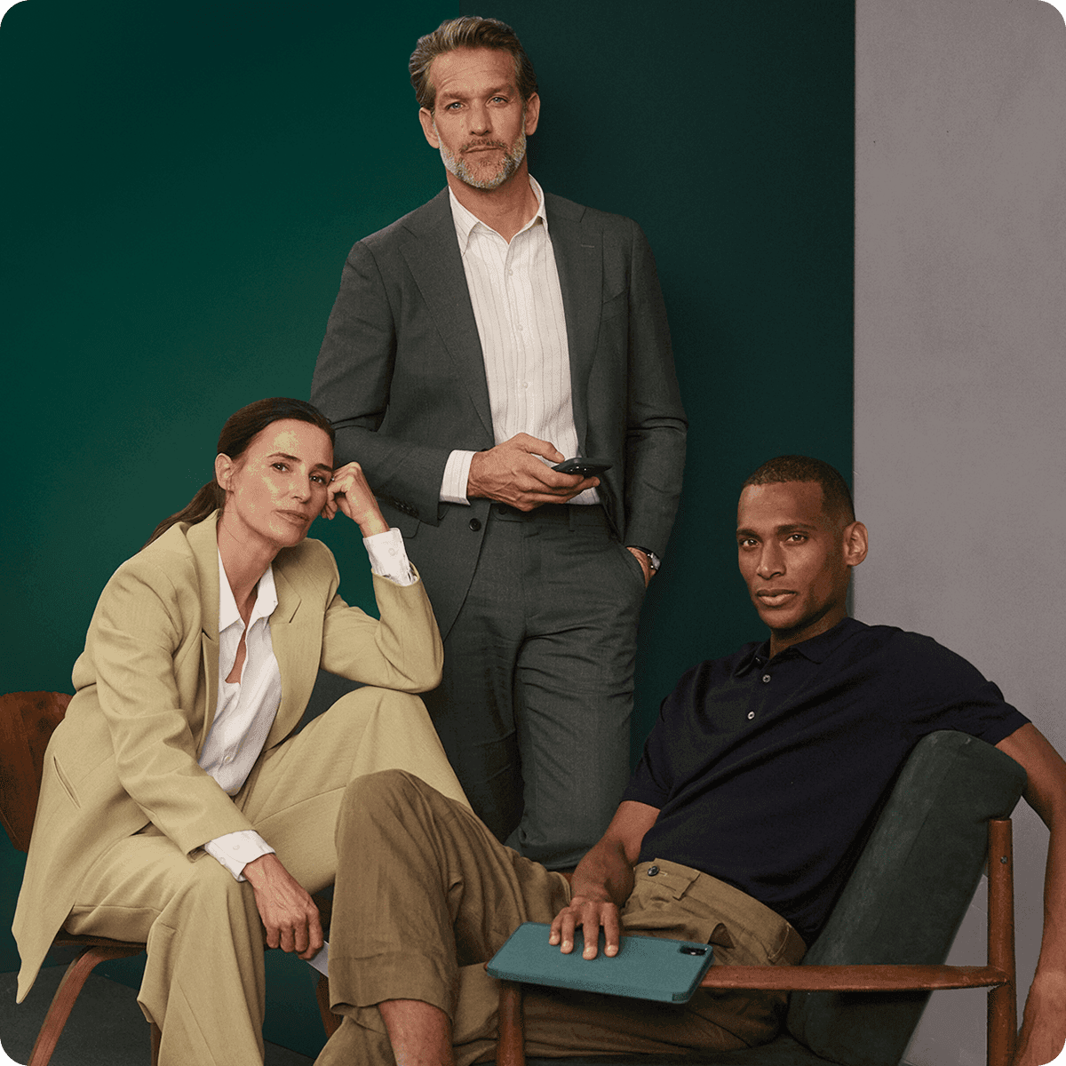 Three people in business attire pose confidently; one seated with a tablet, another standing, and the third seated with her chin on her hand.