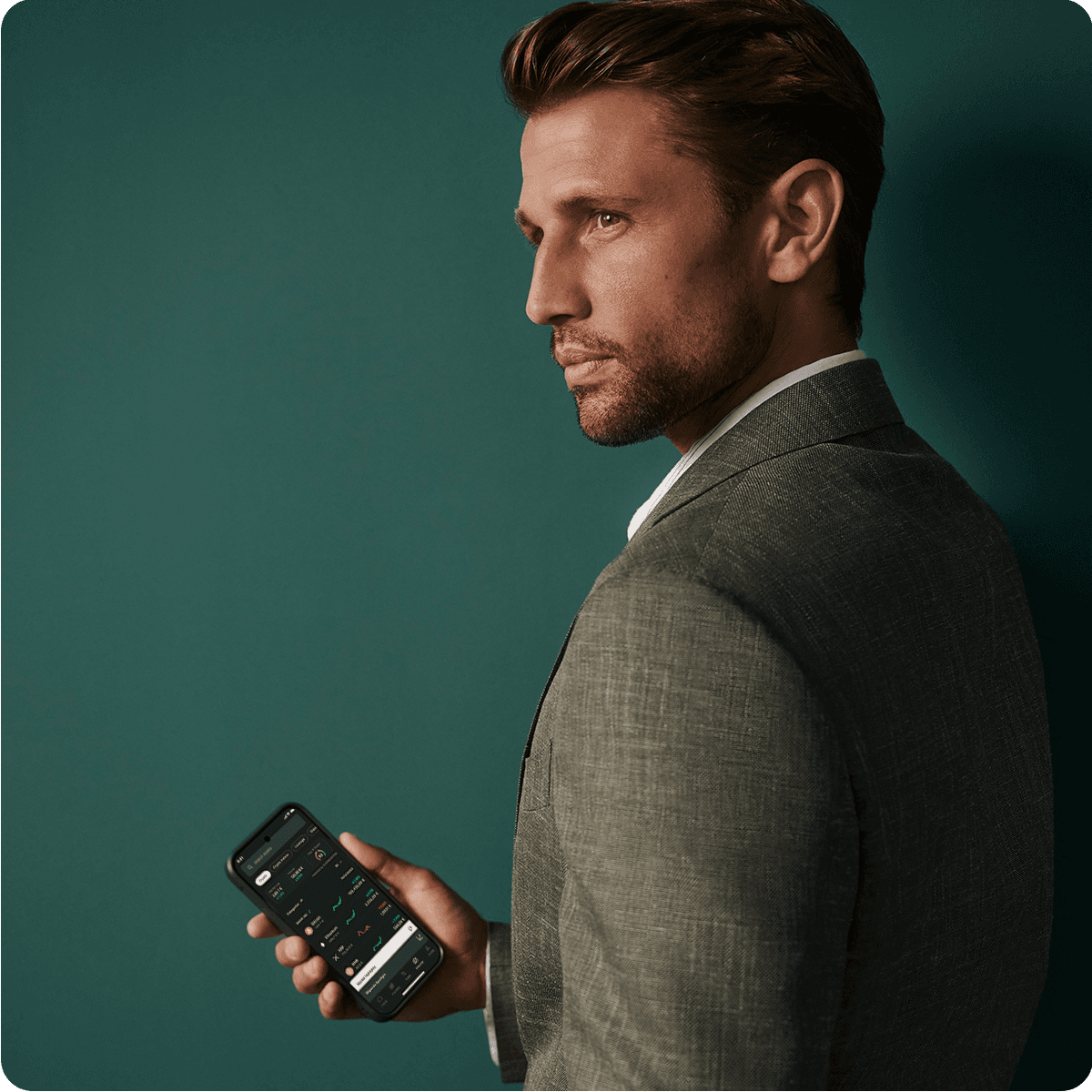 Man in a suit holding a smartphone, looking to the side against a dark green background.
