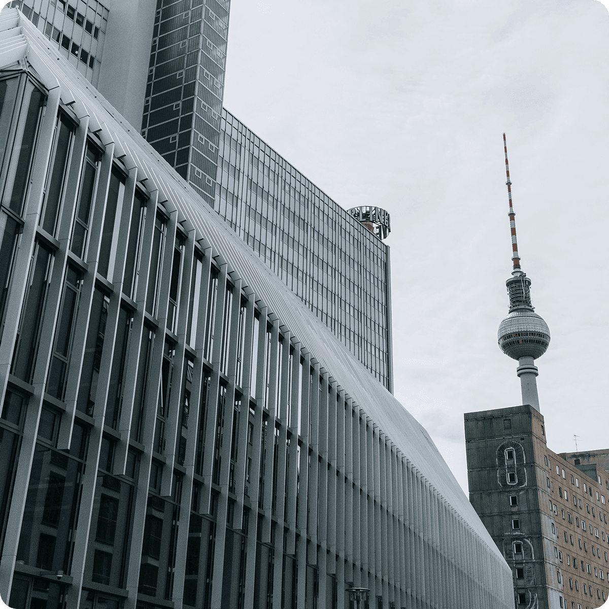 Cityscape featuring modern buildings and the Berlin TV Tower under a cloudy sky.