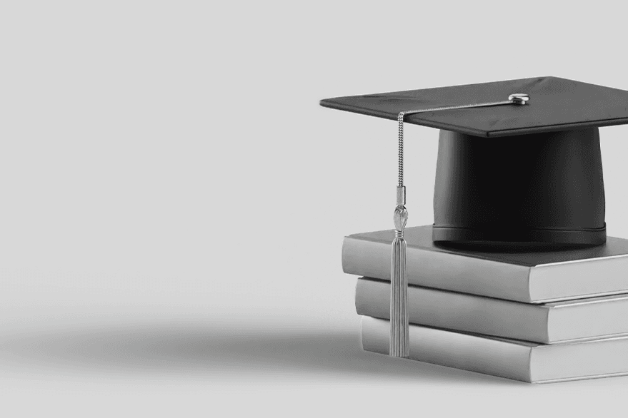 Black graduation cap with tassel resting on a stack of three closed books against a plain light gray background.