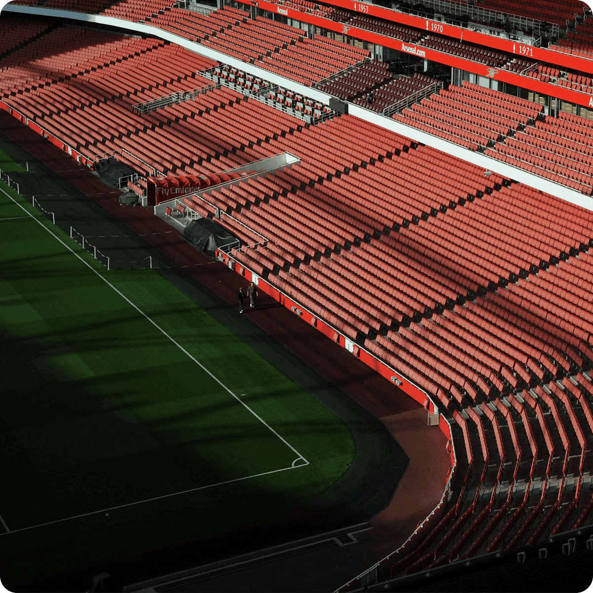 Empty stadium with rows of red seats, partially shaded, overlooking a green football field.