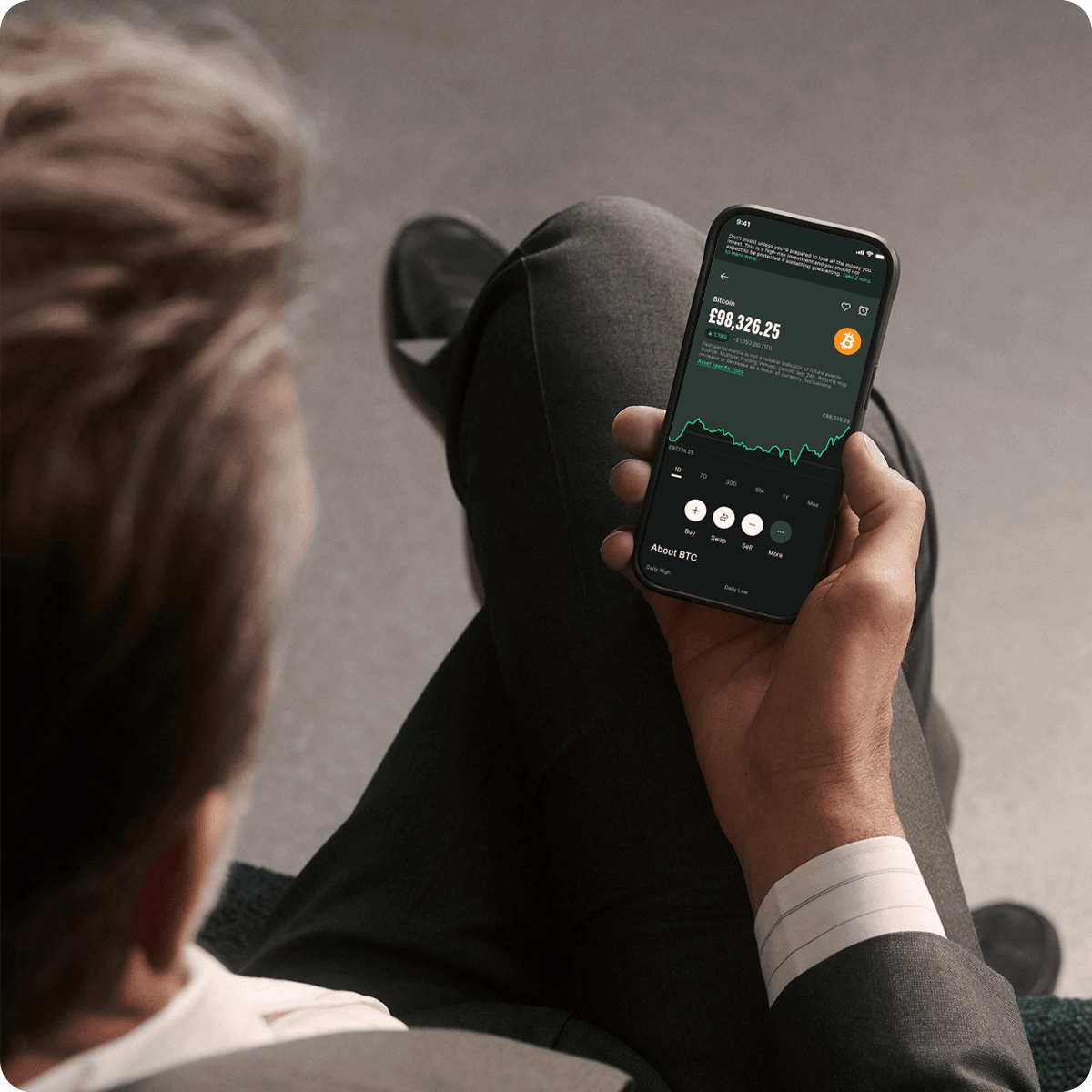 Person in a suit viewing cryptocurrency data on a smartphone, showing a graph and numerical values.