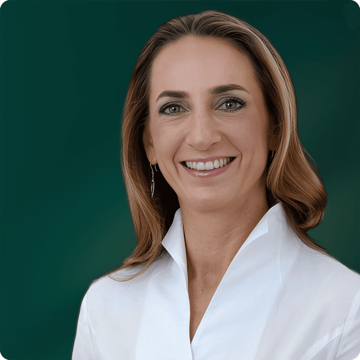 Smiling woman with long light brown hair in a white collared shirt against a dark green background.