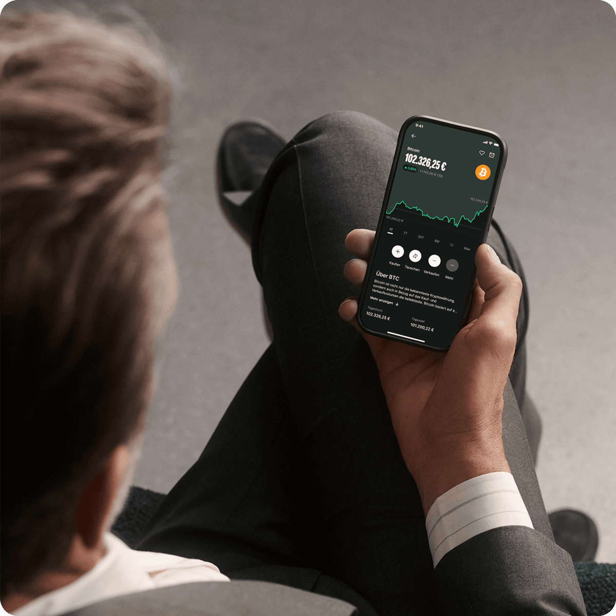 Person in a suit holding a smartphone displaying a cryptocurrency trading app with graphs and data.