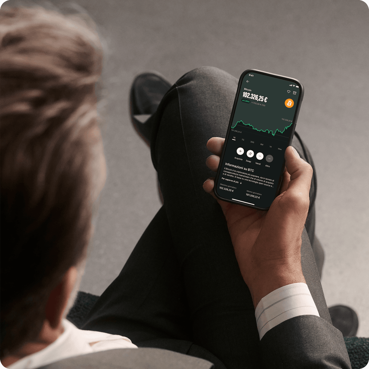 Person in a suit holding a smartphone displaying a cryptocurrency trading app with graphs and data.